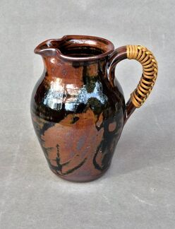 A Sycamore Pottery pitcher with wicker handle
